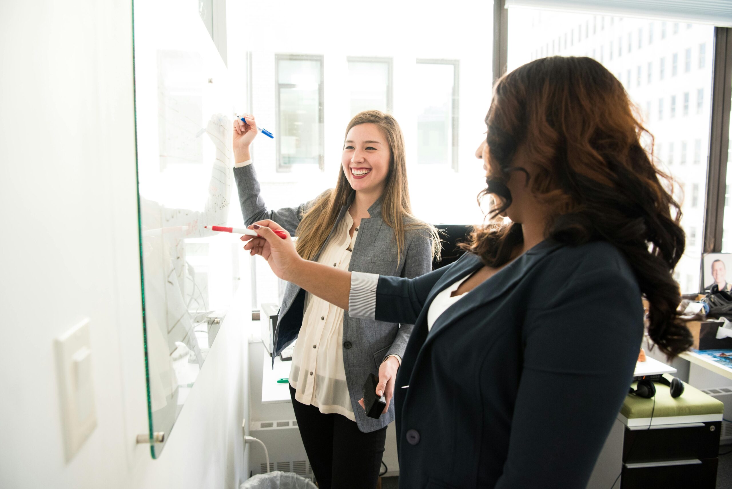 Two saleswomen writing on a dry-erase board.